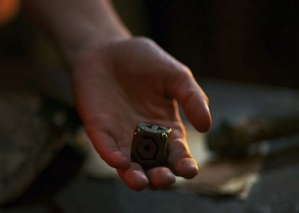 A castaway's open hand holding the small Shot in the Dark die