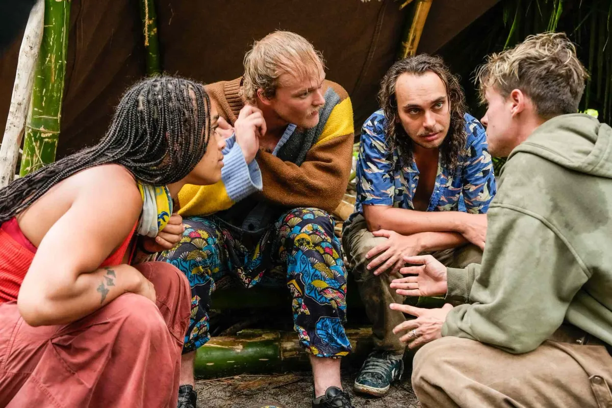 Four Survivor 51 castaways crouched together talking outside a camp shelter in Episode 3
