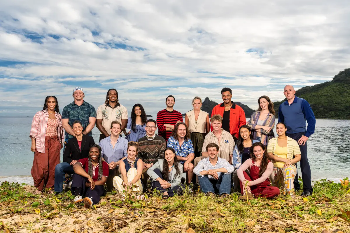 The 21 castaways of Survivor 51 posed together on a beach, with islands behind them