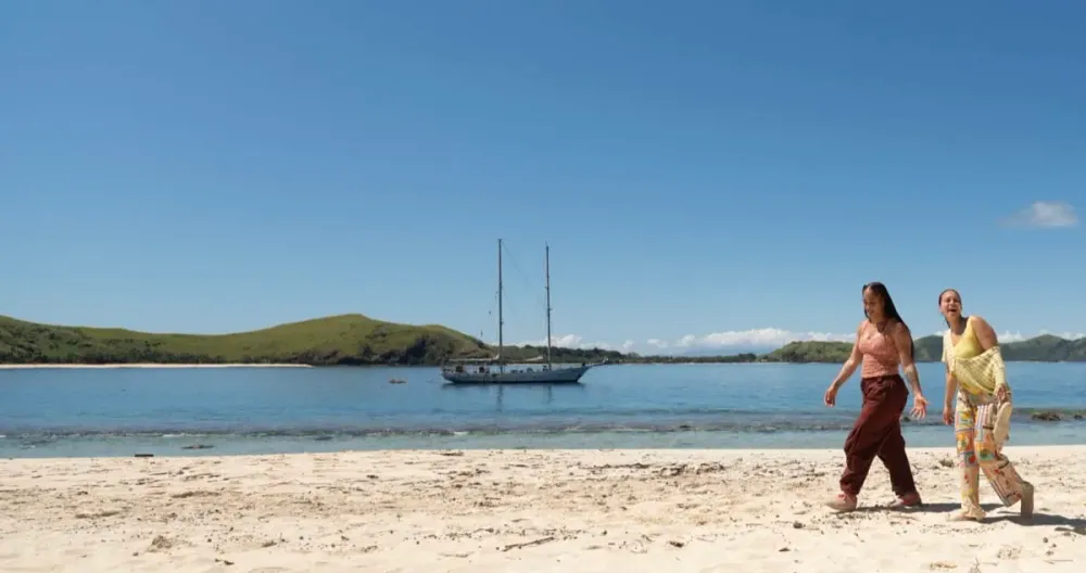 Angelica “Jelly” Loblack and Aaliyah Puglia walking along a Mamanuca beach, with the boat anchored offshore