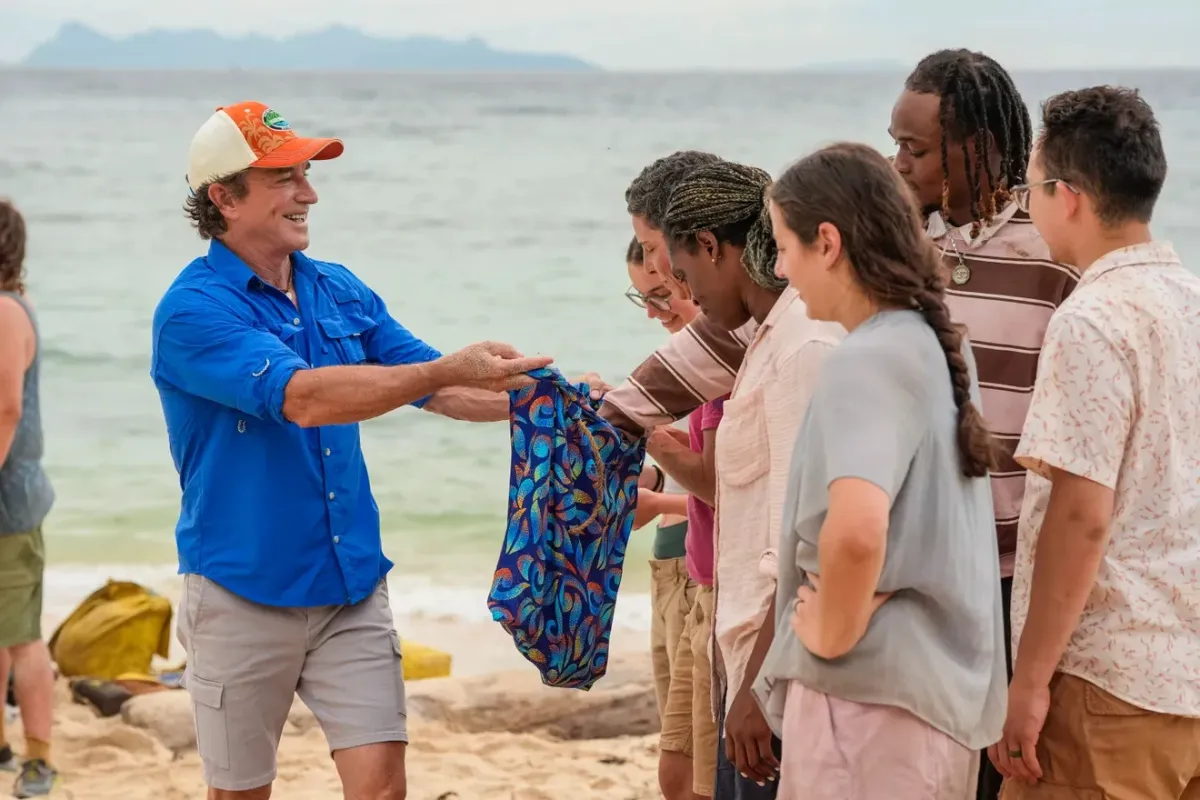Jeff Probst holding out new buffs to Survivor 51 castaways on the beach during the Episode 4 tribe swap